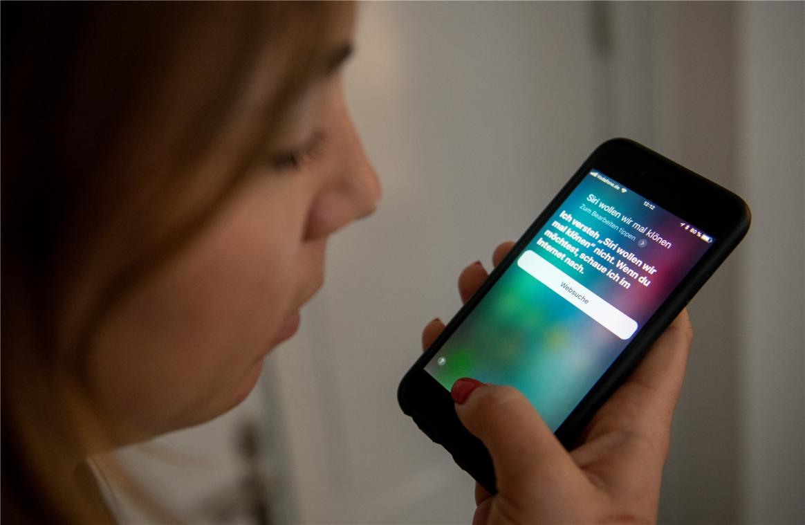 <p>Eine junge Frau bedient auf einem iPhone die Spracherkennung des Apple-Programms Siri.</p>