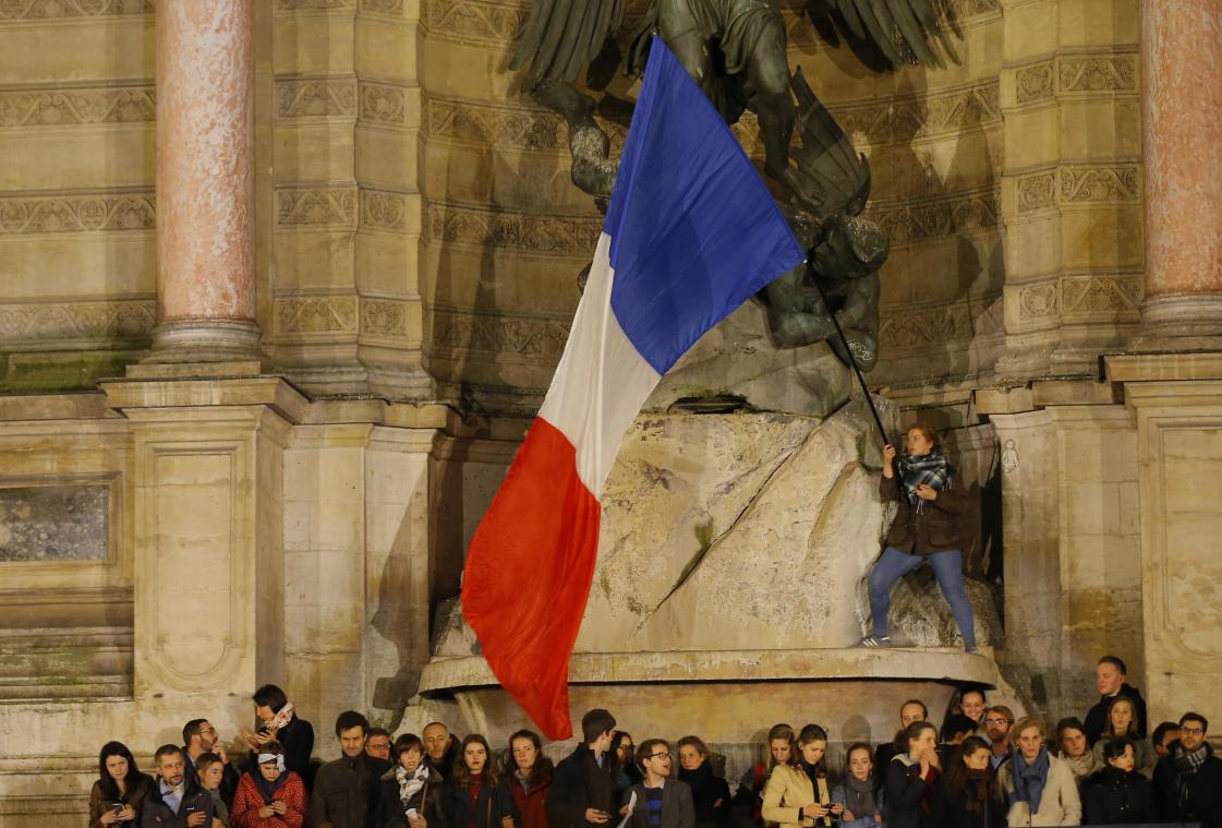 <p>Menschen nehmen an einer Mahwache teil. Ein Mann schwenkt eine französische Fahne.</p>