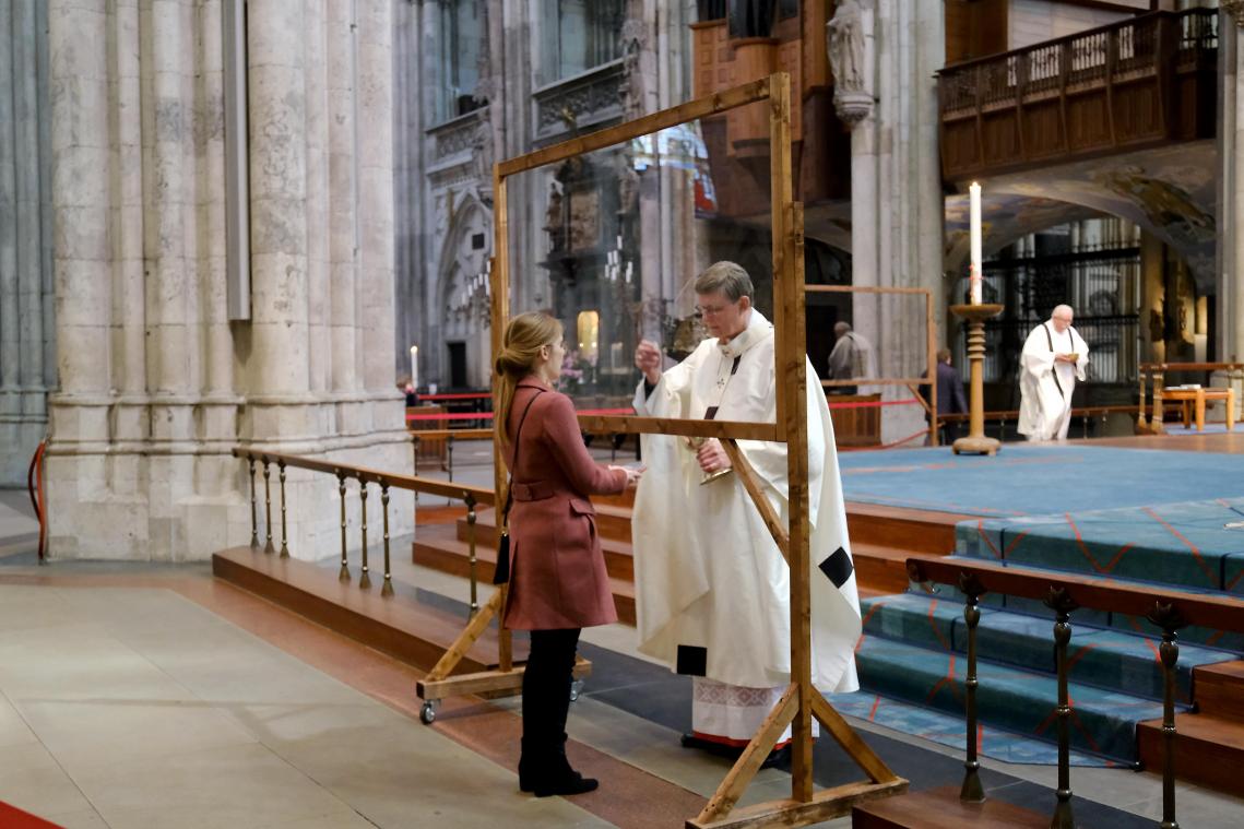 <p>Kardinal Woelki verteilt während der Messe im Kölner dom hinter einer Schutzvorrichtung die Heilige Kommunion.</p>
