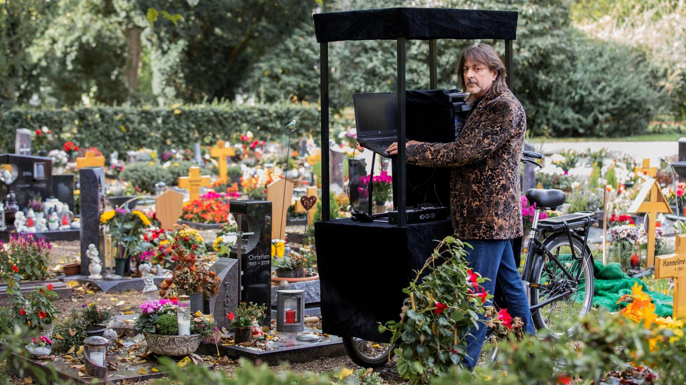 <p>Theo Fitsos, Disc Jockey (DJ), steht mit seiner Musikanlage auf einem Lastenfahrrad neben einem frisch ausgehobenen Grab unmittelbar vor seinem Einsatz bei einer Beerdigung.</p>