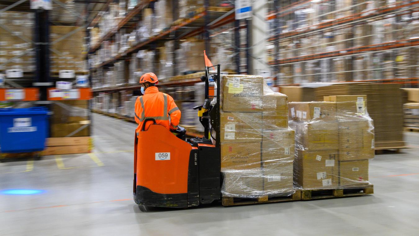 <p>Ein Mitarbeiter des Amazon Logistikzentrums fährt mit Paketen an Hochregalen vorbei.</p>