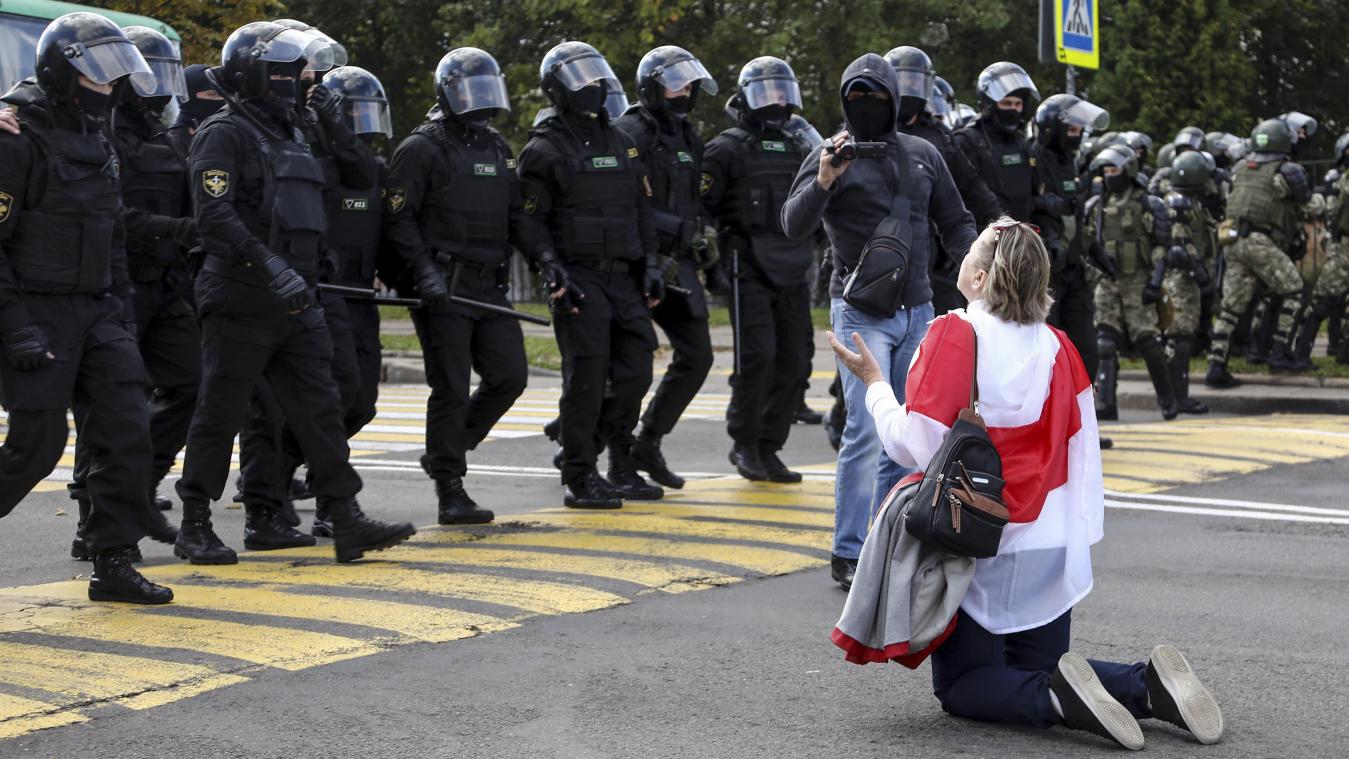 <p>Eine Demonstrantin, die sich eine historische Flagge von Belarus um die Schultern gehängt hat, kniet vor einer Reihe von Polizisten in schwerer Montur auf dem Boden.</p>