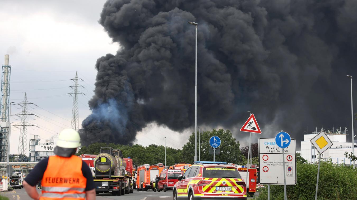 <p>Einsatzfahrzeuge der Feuerwehr unweit einer Zufahrt zum Chemiepark, über dem eine dunkle Rauchwolke aufsteigt. Am 27. Juli 2021 war es in Leverkusen zu einer verheerenden Explosion gekommen. Sieben Mitarbeiter starben, viele wurden verletzt.</p>