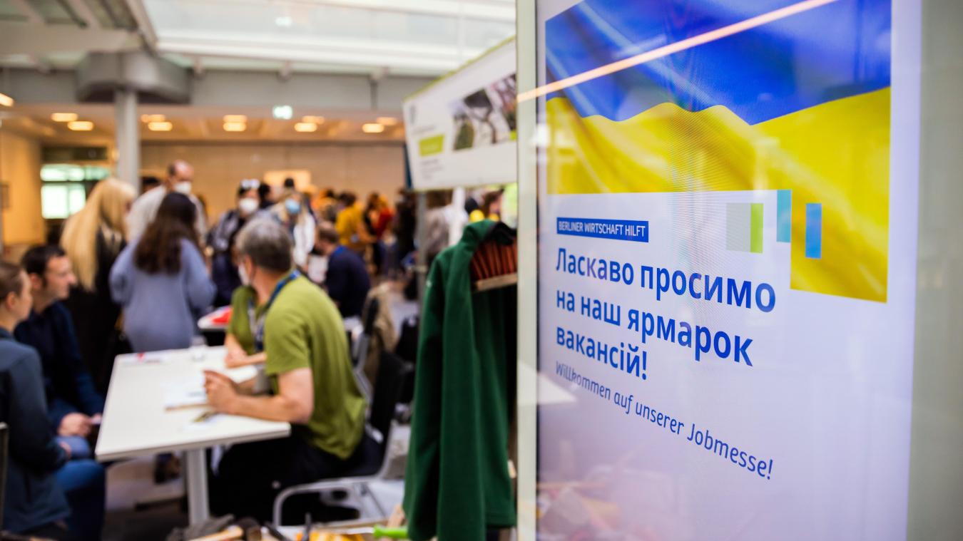 <p>Menschen unterhalten sich bei einer Jobmesse für ukrainische Geflüchtete von der IHK Berlin und der Agentur für Arbeit an einem Infostand.</p>