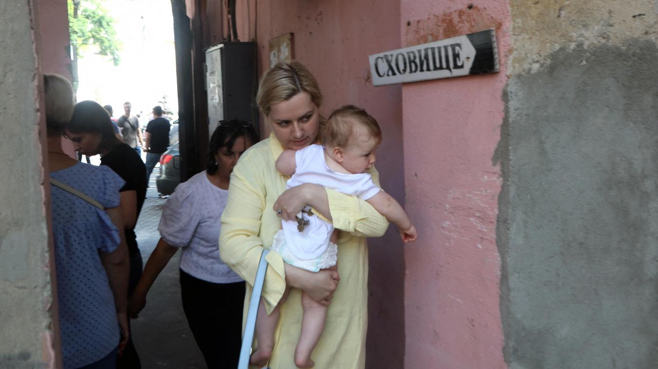 <p>Eine junge Frau trägt ein Baby, während sie in Odessa an einem Schild „Unterkunft“ vorbeigeht.</p>
