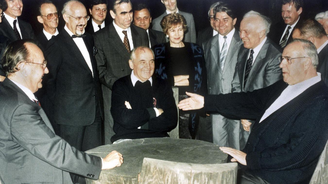 <p>Der damalige Bundeskanzler Helmut Kohl (r.), der damalige sowjetische Staatspräsident Michail Gorbatschow (Mitte) und der damalige Bundesaußenminister Hans-Dietrich Genscher (l.) unterhalten sich am 15. Juli 1990 an einem rustikalen Arbeitstisch in Archys, Russland. Im Hintergrund rechts von Gorbatschow steht seine Frau Raissa.</p>