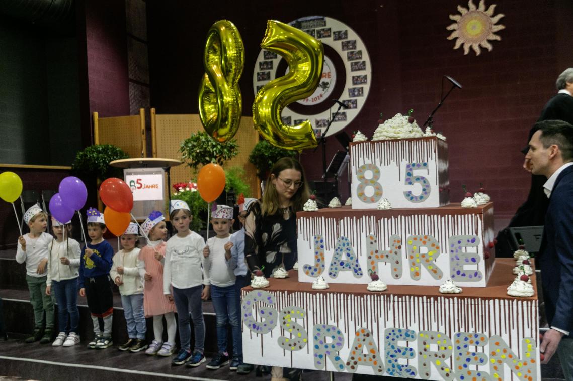 <p>Eine große Torte aus Pappe bringen die Kindergartenkinder auf die Bühne der Gemeindeschule.</p>