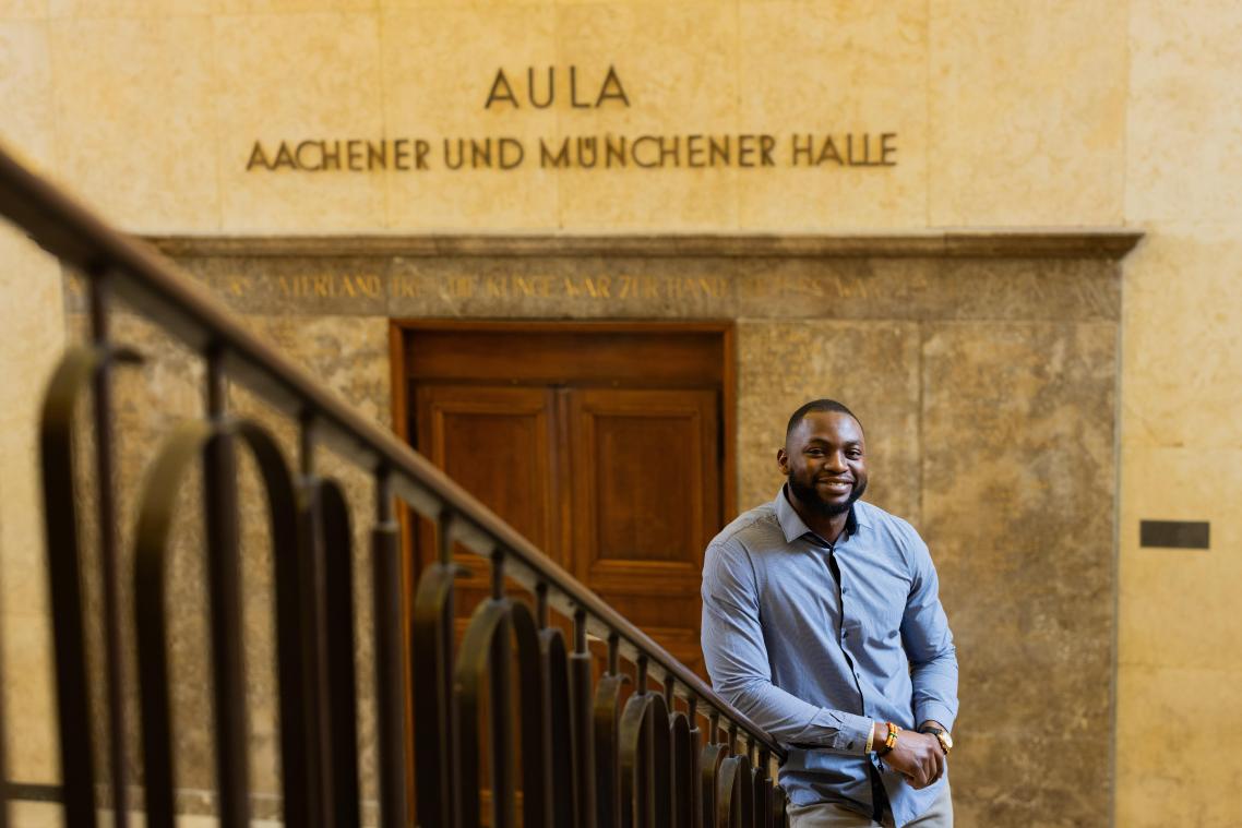 <p>Contimi Kenfack Mouafo, Student der Elektrotechnik an der RWTH Aachen, steht in einem Universitätsgebäude. Der 28-Jährige engagiert sich mit dem Verein „3 E’s 4 Africa“.</p>