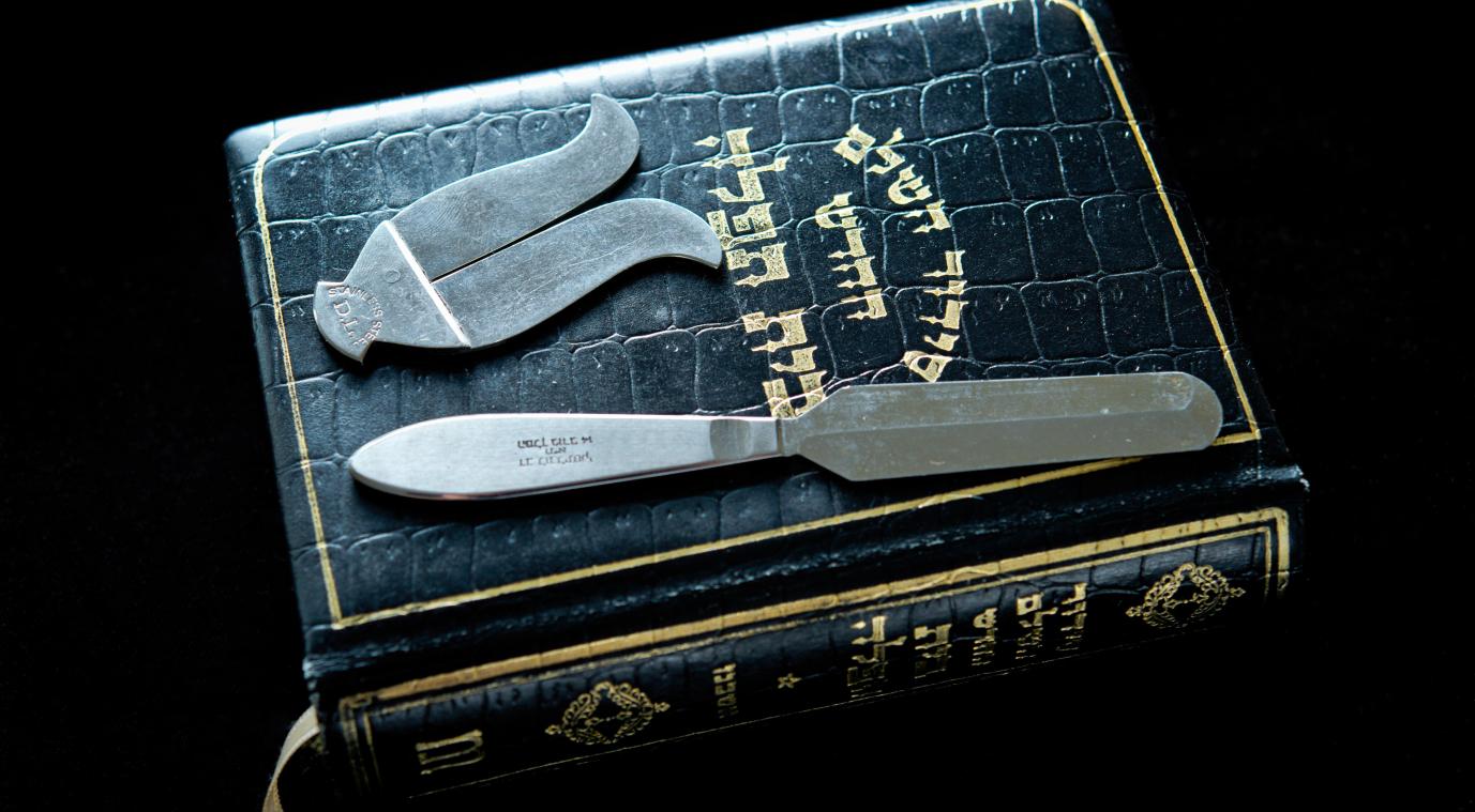 <p>Beschneidungsbesteck, ein Messer und ein Vorhautschutz, auf einem jüdischen Gebetsbuch</p>