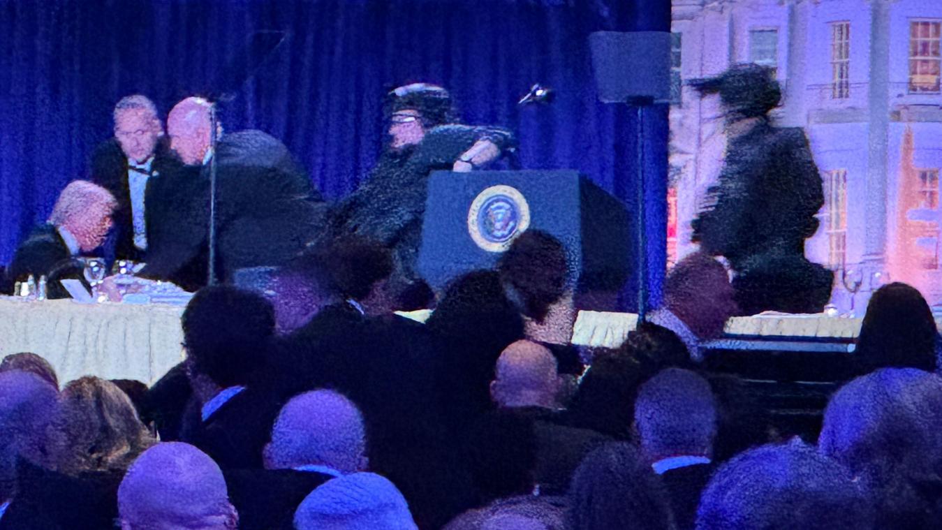 <p>US-Präsident Donald Trump (l.) sitzt auf der Bühne, während Agenten des US-Geheimdienstes ihn nach einem Vorfall außerhalb des Ballsaals während des White House Correspondents' Dinner aus dem Ballsaal bringen.</p>