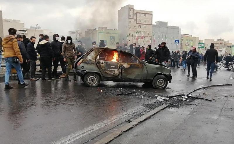 <p>Demonstranten versammeln sich um ein brennendes Auto.</p>