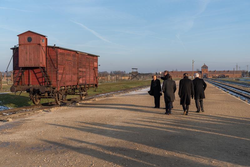 <p>Merkel steht vor einen Güterwagen, im Hintergrund ist das Eingangsportal des Lagers zu sehen.</p>