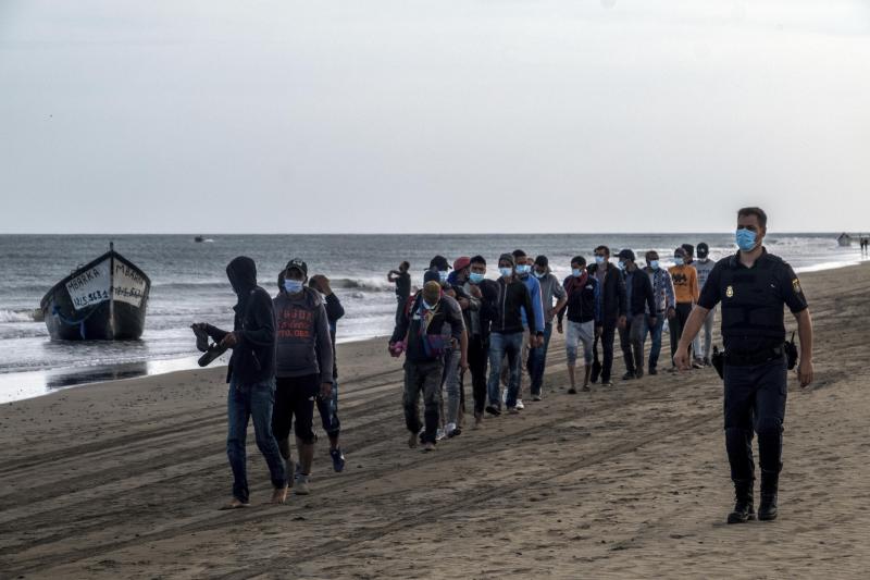 <p>Migranten aus Marokko gehen in Begleitung der spanischen Polizei am Strand entlang, nachdem sie mit einem Holzboot an der Küste von Gran Canaria angekommen sind.</p>