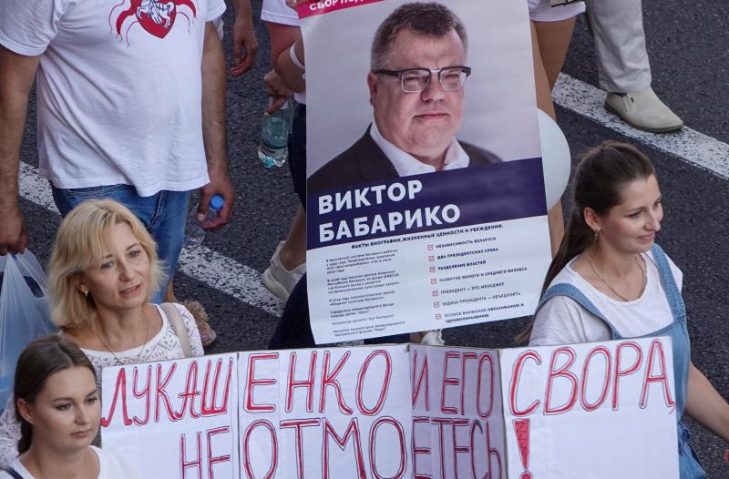 <p>Menschen gehen auf dem Platz der Unabhängigkeit bei einer Demonstration gegen Machthaber Lukschenko und tragen ein Transparent mit dem Foto von Viktor Babariko, der bei der Präsidentenwahl gegen Lukaschenko antreten wollte.</p>