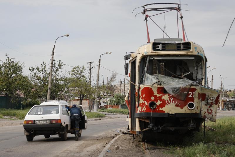 <p>Ein Mann schiebt ein liegengebliebenes Auto an einer beschädigten Straßenbahn im Gebiet der Volksrepublik Donezk im Osten der Ukraine vorbei.</p>
