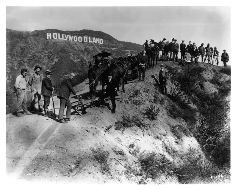 <p>Menschen stehen vor dem übergroßen Schriftzug „Hollywoodland“, der 1923 von einer Maklerfirma für Grundstücke als Werbegag in den damals unbewohnten Hügeln aufgestellt worden ist.</p>