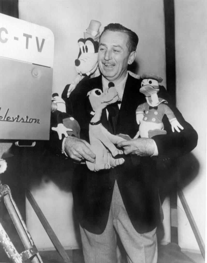 <p>Der amerikanische Filmproduzent Walt Disney vor einer Fernsehkamera mit seinen Figuren Pluto (Mitte) und Donald Duck (rechts) im Arm.</p>