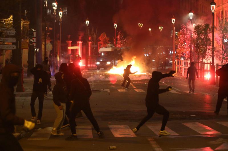 <p>Demonstranten auf Korsika werfen Steine und Fackeln auf französische Gendarmen, während im Hintergrund ein Feuer brennt.</p>