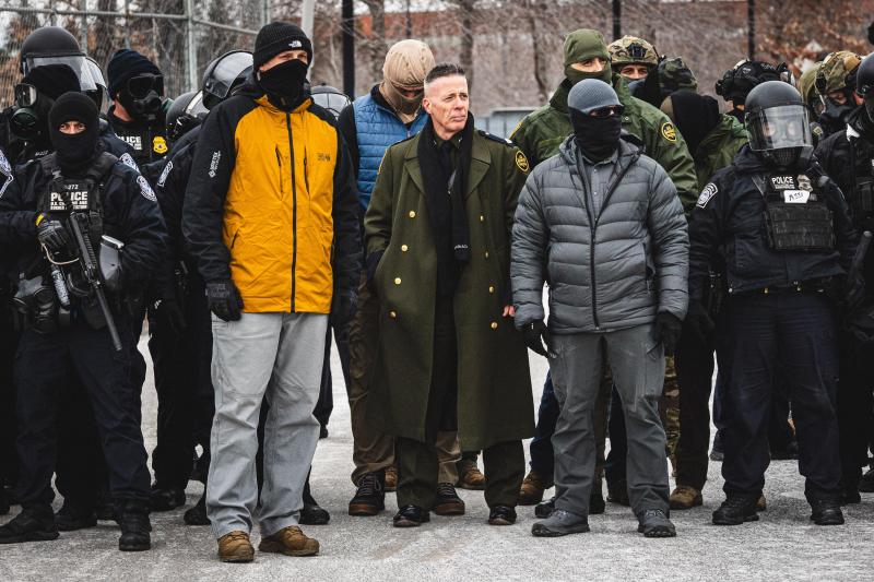 <p>Gregory Bovino (Bildmitte)beobachtet einen Protest, während sich Gemeindemitglieder am Eingang des Whipple-Gebäudes in Minneapolis versammeln, um sich mit ihren Nachbarn zu solidarisieren, die von ICE-Agenten festgehalten werden.</p>