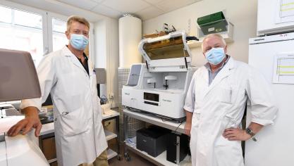 <p>Dr. Frédéric Marenne (links) und Laborleiter Paul Göbbels (rechts) vor einem hochmodernen Analysegerät zum Nachweis von Covid-19-Antikörpern.</p>