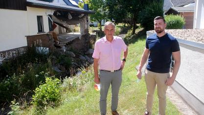 <p>Hellenthals Bürgermeister Rudolf Westerburg (links) und sein für die Abwicklung der Hochwasserschäden zuständiger Mitarbeiter Jonathan Klein vor einem schwer beschädigten Wohnhaus im Ortsteil Reifferscheid-Wiesen.</p>