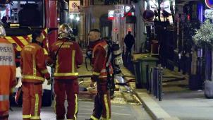 <p>Das Videostandbild zeigt Feuerwehrleute im Einsatz in einer Seitenstraße in der Nähe eines brennenden Mehrfamilienhauses.</p>