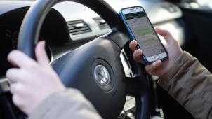 <p>Eine Autofahrerin liest während der Fahrt Nachrichten auf ihrem Smartphone.</p>
