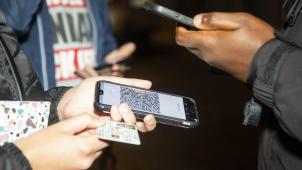 <p>Am Eingang einer Kneipe in Brüssel scann ein Türsteher (r.) das digitale CST eines Kunden und gleicht es mit den Daten auf dessen Personalausweis ab.</p>