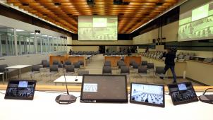 <p>Der am Montag begonnene Prozess gilt gleichzeitig als Generalprobe für den großen Terrorprozess zu den Brüsseler Anschlägen von März 2016, der ab Oktober ebenfalls im neuen Gerichtsgebäude „Justitia“ in Haren stattfinden wird. Bild: der Verhandlungssaal aus Sicht der Richter, links die Hochsicherheitsboxen für die Angeklagten.</p>