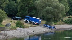 <p>Ein Leichenwagen und ein Fahrzeug mit Boot des Technischen Hilfswerks (THW) stehen am Eiserbachsee.</p>