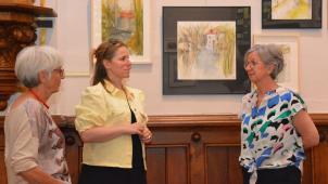 <p>In der Bergkapelle erfreut sich Ministerin Isabelle Weykmans an den spürbar luftigen, frischen Motiven, die Petra Michel-Neumann (rechts) und Claudine Mertens (links) den Ecken und Winkeln der Unterstadt widmen.</p>