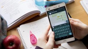 <p>Eine Schülerin sitzt mit ihrem Handy und ihren Schulsachen an einem Schreibtisch.</p>