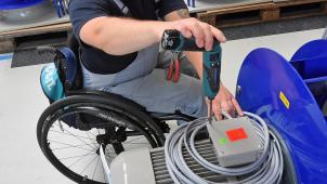 <p>An einem Arbeitsplatz für Motorklemmen ist ein Mitarbeiter im Rollstuhl mit Montagearbeiten beschäftigt.</p>