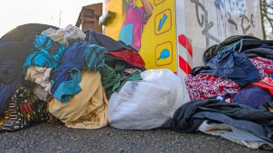 <p>Gebrauchte Kleidungsstücke liegen vor einem Sammelcontainer für Altkleider.</p>