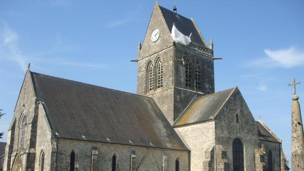 <p>Sainte-Mère-Eglise wurde berühmt durch die amerikanische Luftlandung. Ein US-Soldat blieb damals am Kirchturm hängen. Heute erinnern eine Puppe und ein weißer Fallschirm an die Ereignisse.</p>