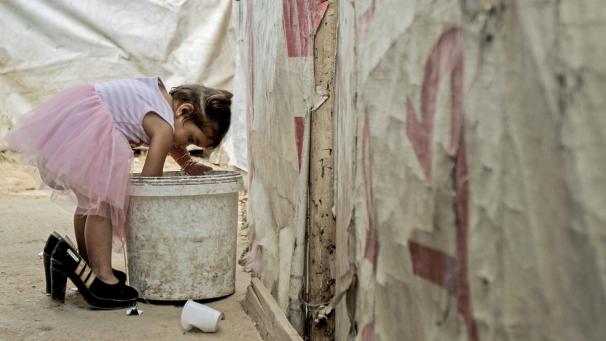 <p>Ein syrisches Flüchtlingsmädchen trägt ein Paar Absatzschuhe, während sie in einem Flüchtlingscamp im Libanon in einen Mülleimer greift.</p>