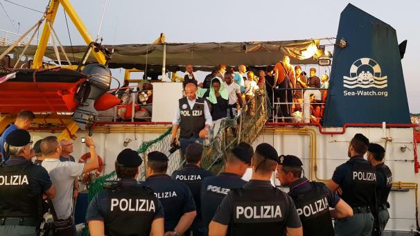 <p>Migranten gehen von Bord des Rettungsschiffs „Sea-Watch 3“ im Hafen der Insel Lampedusa. Das Schiff der deutschen Hilfsorganisation Sea-Watch ist nach dem unerlaubten Anlegen im Hafen der italienischen Insel Lampedusa und der Festnahme der Kapitänin beschlagnahmt worden. Das bestätigte ein Sea-Watch-Sprecher.</p>