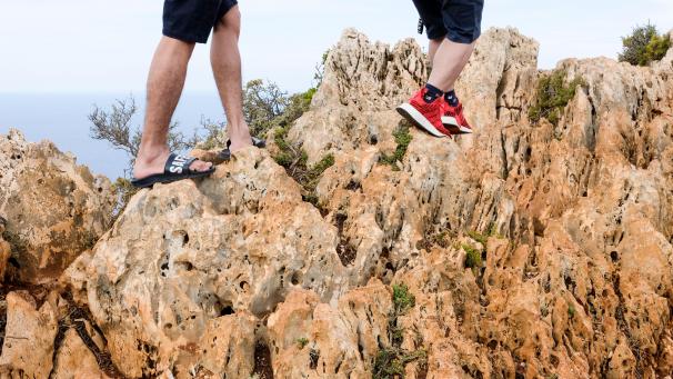 <p>Urlauber gehen mit Sportschuhen und Badelatschen auf felsigem Gelände an einer Steilküse am Meer entlang. Manche Touristen lassen sich in den Ferien auf allzu gewagte Dinge ein.</p>