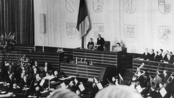 <p>7. September 1949: Alterspräsident Paul Löbe (Mitte), spricht während der konstituierenden Sitzung des Deutschen Bundestages in der einstigen Turnhalle der Pädagogischen Akademie, die zuvor zum Plenarsaal umgebaut worden war.</p>