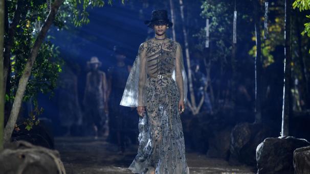 <p>Ein Model präsentiert eine Kreation von Dior auf einem Laufsteg geziert mit Bäumen.</p>
