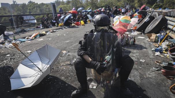 <p>Ein Teilnehmer einer Demonstration sitz in Schutzkleidung und mit einem Molotow-Cocktail auf einer Brücke vor dem Campus der chinesischen Universität.</p>