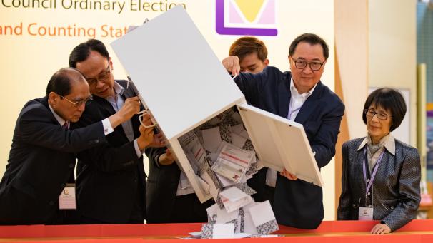 <p>Barnabas Fung (2.v.r), Vorsitzender der Wahlkommission EAC, schüttet in einem Wahllokal vor der Auszählung die Stimmzettel aus einer Wahlurne aus.</p>