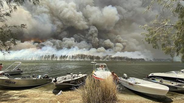 <p>Boote werden an Land gezogen, während im Hintergrund Rauchwolken über dem Ufer hinter dem Canjola See aufsteigen.</p>
