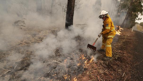 <p>Ein Feuerwehrmann benutzt eine Harke, um brennende Holzteile zu verteilen während er ein Feuer in der Nähe des Burrill Lake bekämpft.</p>