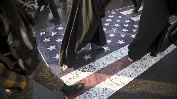 <p>Die Teilnehmer einer Trauerzeremonie für den getöteten General Soleimani laufen über eine auf der Straße liegenden Flagge der USA.</p>