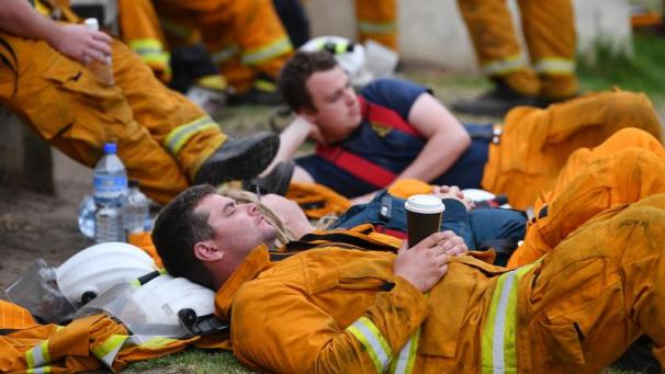 <p>Erschöpfte Feuerwehrleute liegen am Boden.</p>