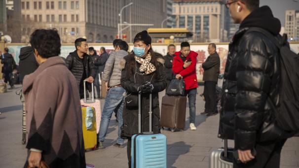 <p>Eine Reisende steht mit einem Rollkoffer in der Nähe des des Pekinger Bahnhofs und trägt einen Mundschutz. Die Ausbreitung der rätselhaften Lungenkrankheit in China ist möglicherweise</p>