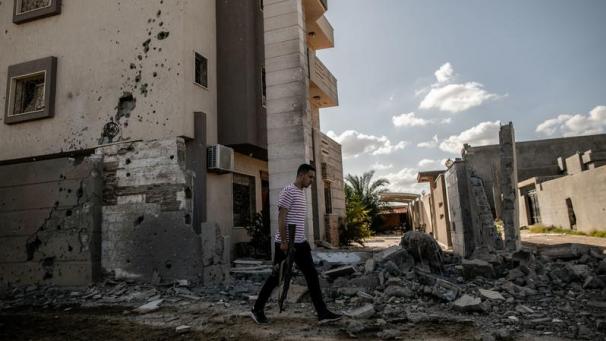 <p>Ein Mann mit Gewehr geht an einem zerstörten Haus in einem verlassenen Vorort von Tripolis vorbei. Seit bald neun Jahren tobt in Libyen ein Bürgerkrieg.</p>