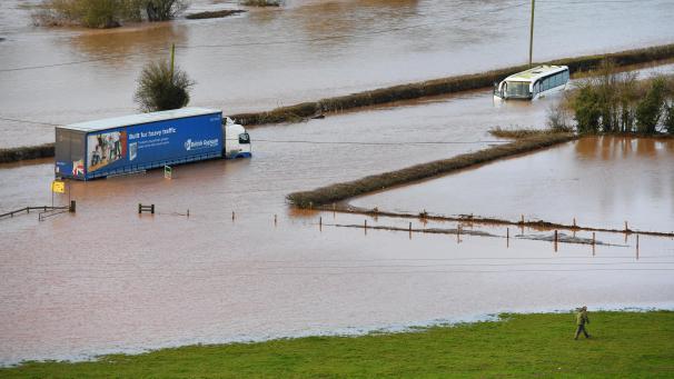 <p>Großbritannien, Lindridge: Ein Lkw (l.) und ein Reisebus stehen auf der A443 in Hochwasser. Das Hochwasser-Risiko in Großbritannien wird nach Experten-Ansicht noch Tage bestehen bleiben.</p>
