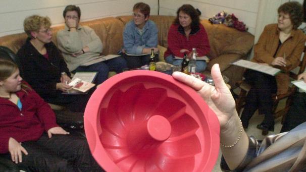 <p>22.11.2002, Nordrhein-Westfalen, Bochum: Eine rote Kunststoffbackform preist eine Tupperware-Beraterin einer Runde von interessierten Kundinnen in einem Wohnzimmer an.</p>